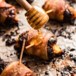Honey being drizzled over freshly baked bacon-wrapped dates on the sheet pan.
