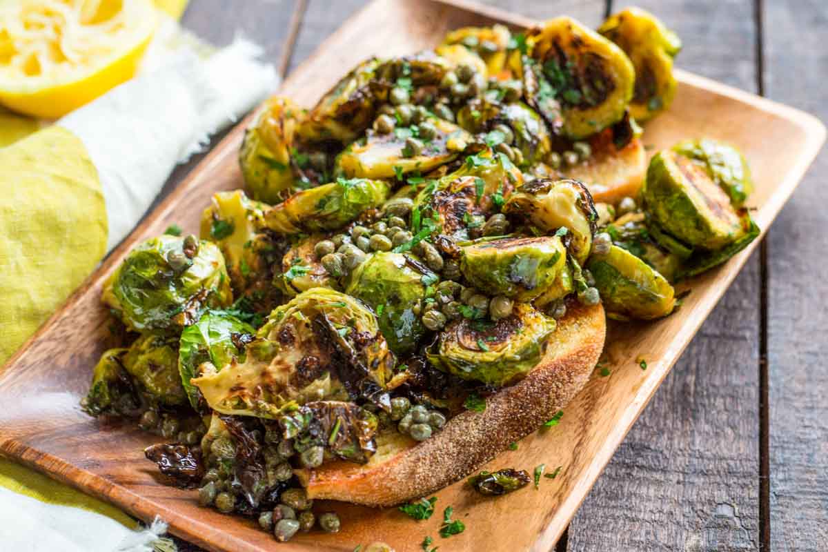 Roasted Brussels sprouts with golden edges and capers served on a toasted slice of Italian bread, drizzled with anchovy butter and sprinkled with parsley.