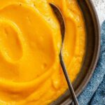 Close-up of smooth, creamy butternut squash puree in a dark bowl with a spoon resting inside.