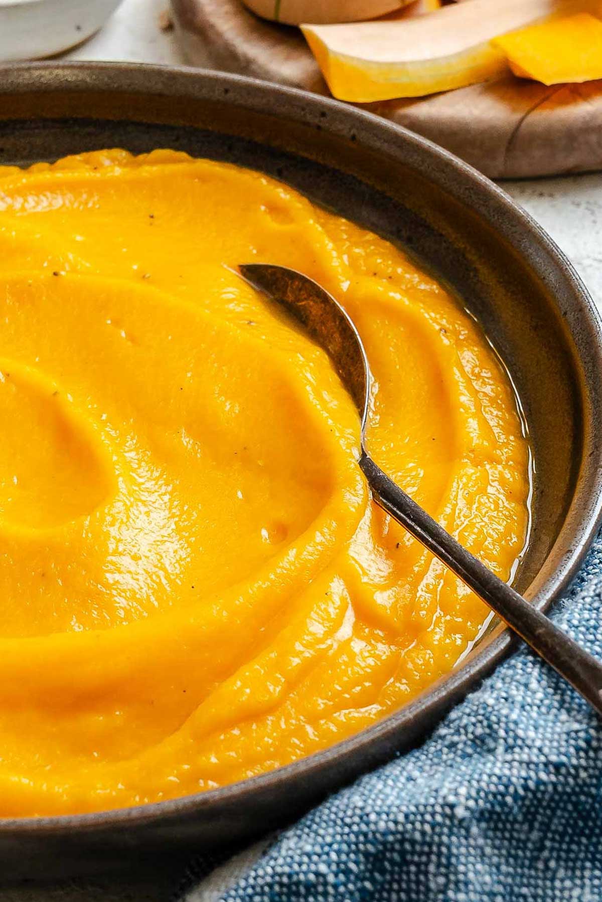 Side angle of silky brown butter squash puree in a shallow bowl, showing its glossy texture and rich orange color.