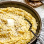 Overhead view of creamy parmesan polenta in a rustic bowl beside parmesan cheese and butter.