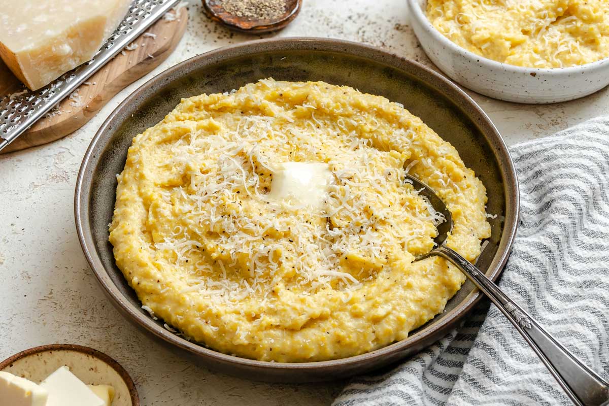 Wide photo of a bowl of parmesan polenta topped with butter and freshly grated cheese, ready to serve.