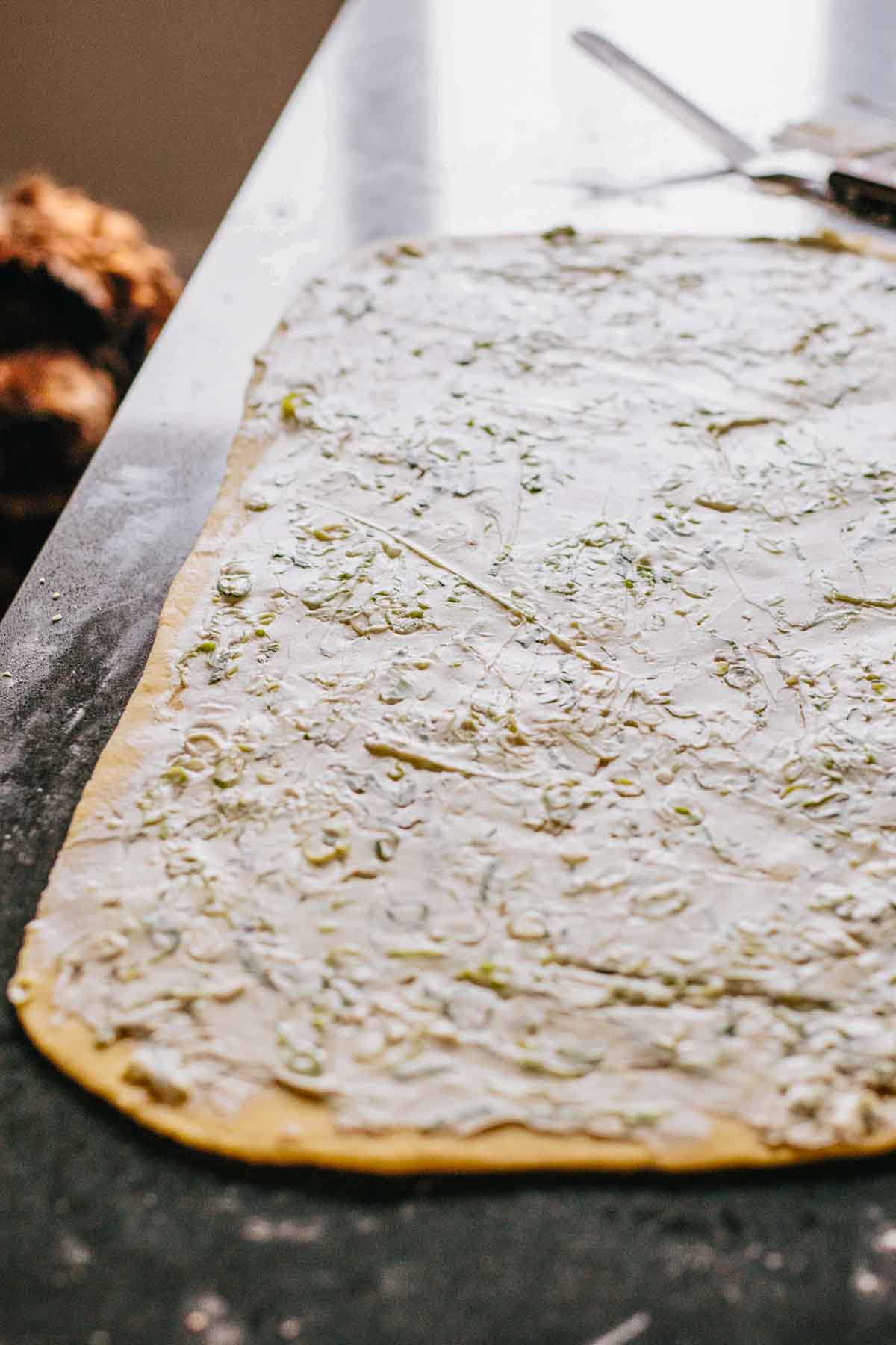 Rolled dough spread with scallion cream cheese before cutting and layering for the pull apart bread.