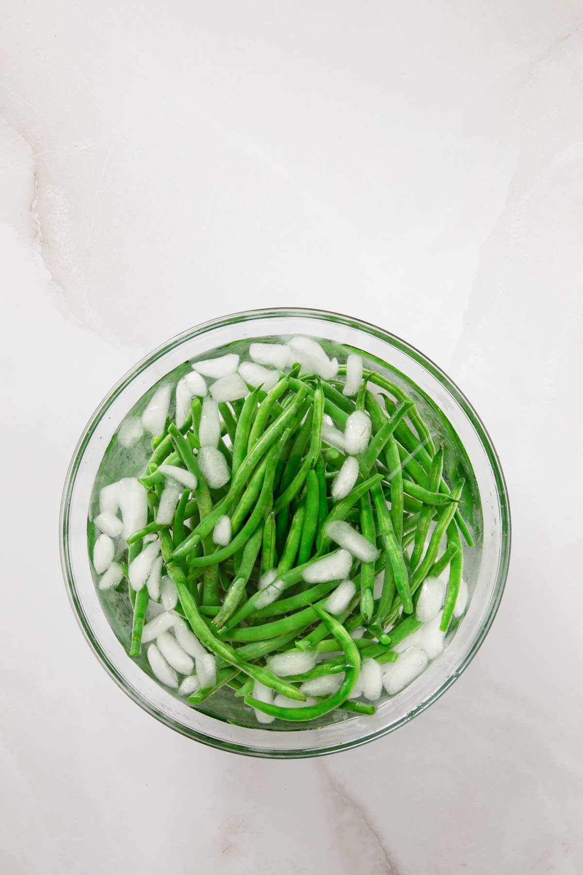 Blanched green beans cooling in a glass bowl filled with ice water to stop the cooking.