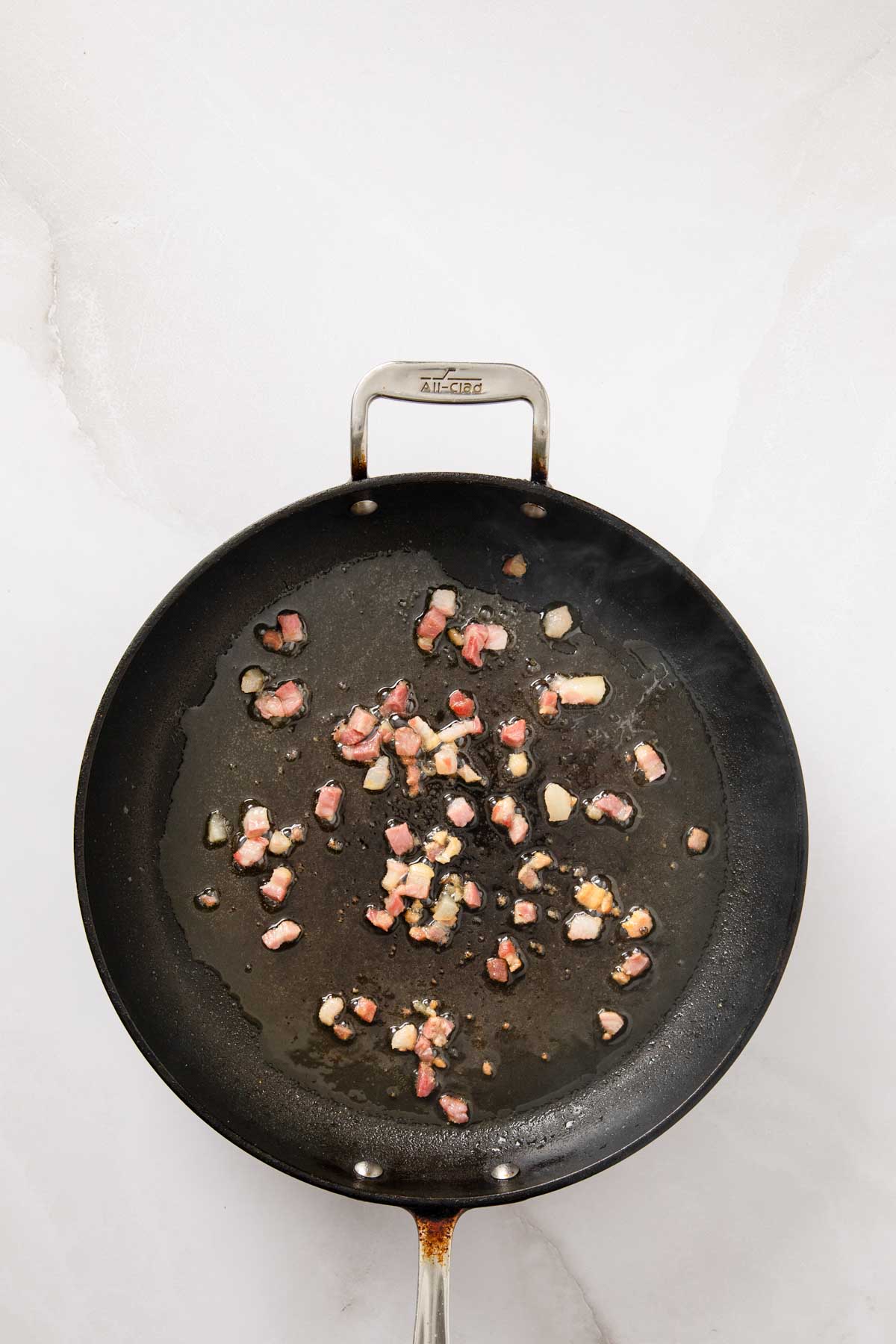 Diced pancetta rendering and turning golden in a black skillet.