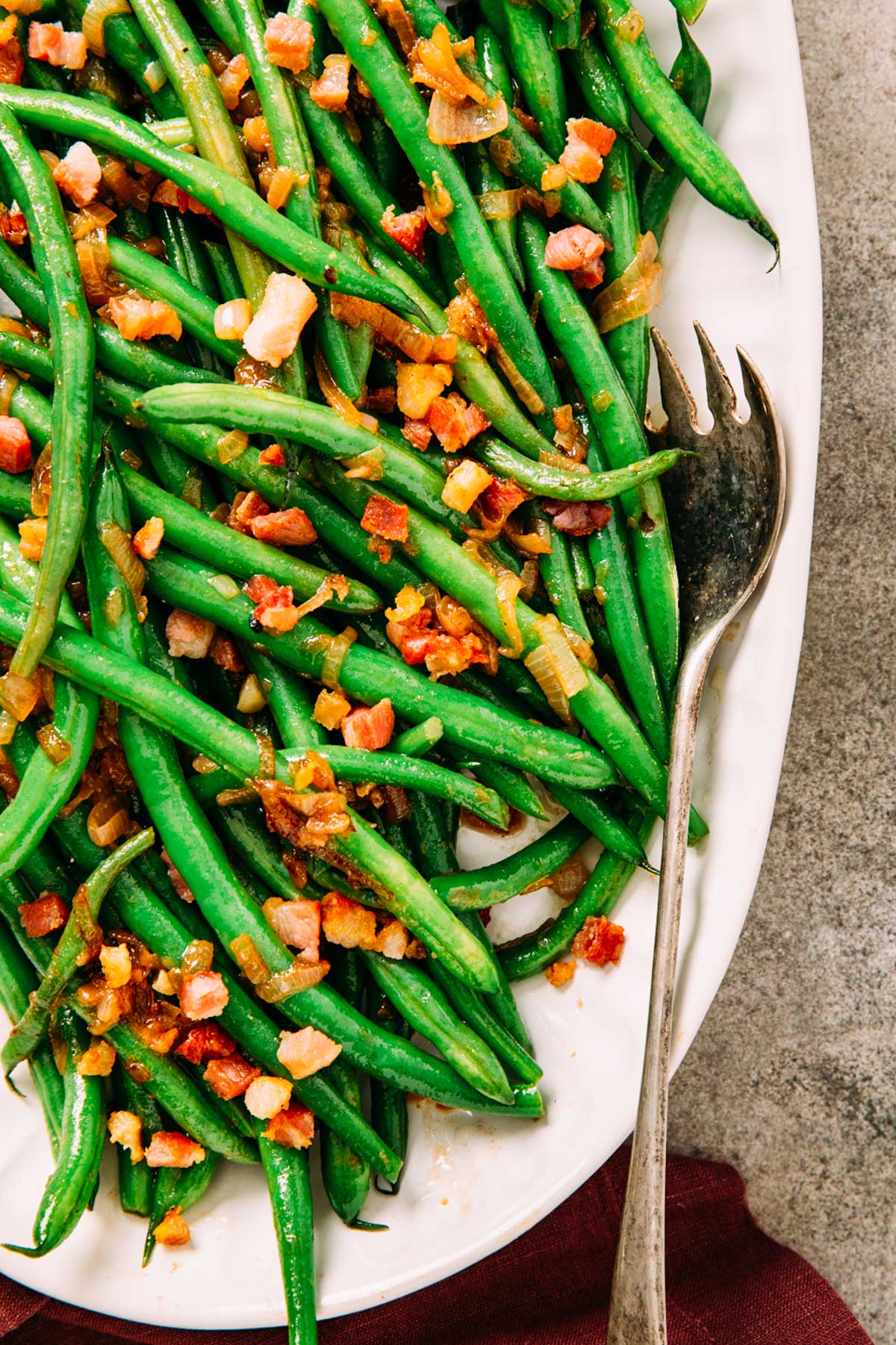 Finished green beans with crispy pancetta and shallots arranged on a white serving platter.