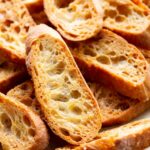 Side angle view of baked crostini stacked on a patterned serving platter lined with parchment paper.