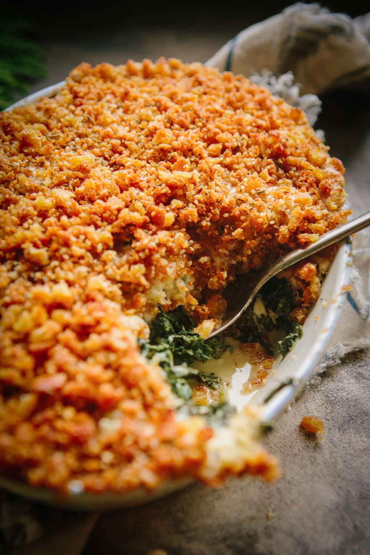 Close-up of a spoonful taken from the kale gratin, highlighting the creamy sauce and layers of wilted kale under the browned breadcrumb crust.