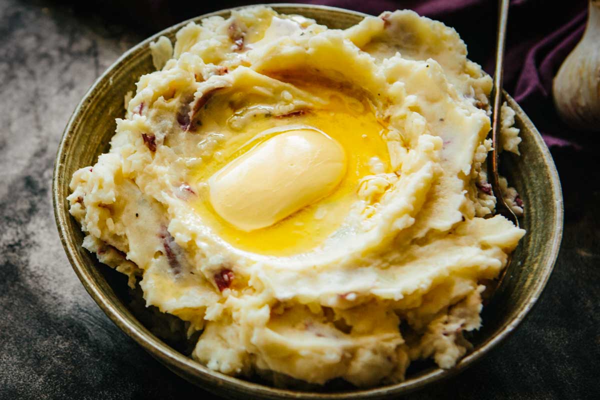 Close-up of mashed potatoes with red skins and melted butter pooling in the center.