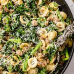 Close-up of orecchiette pasta with broccoli rabe and sausage topped with freshly grated cheese.