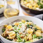 Bowl of orecchiette with broccoli rabe and sausage set on a table with a glass of white wine in the background.