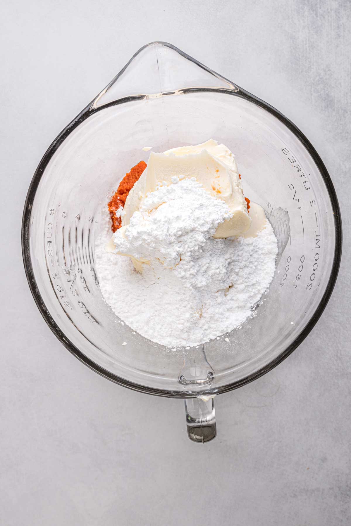 Glass mixing bowl with ricotta, mascarpone, pumpkin puree, and powdered sugar ready to be whipped together for the cannoli filling.