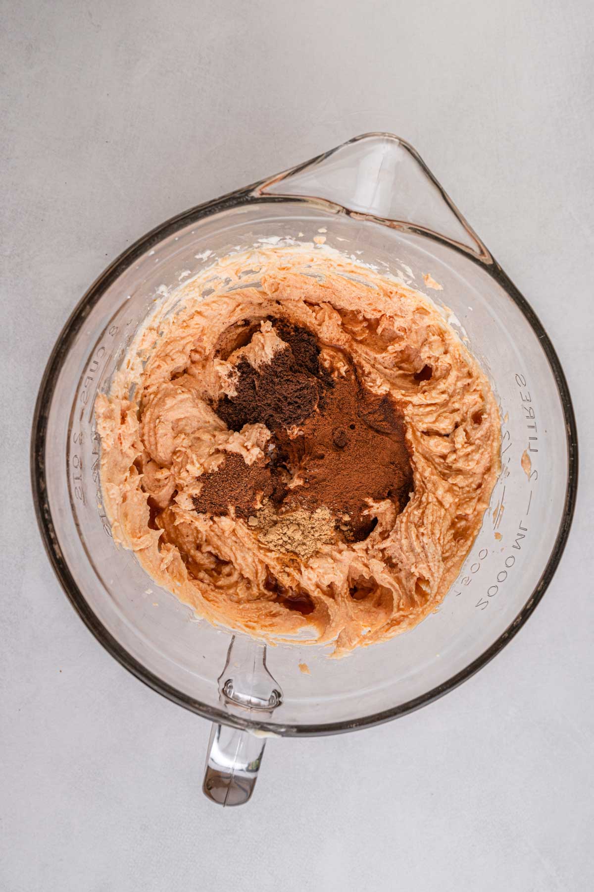Pumpkin cannoli filling in a glass bowl with warm spices-cinnamon, nutmeg, ginger, and cloves-added on top before mixing.