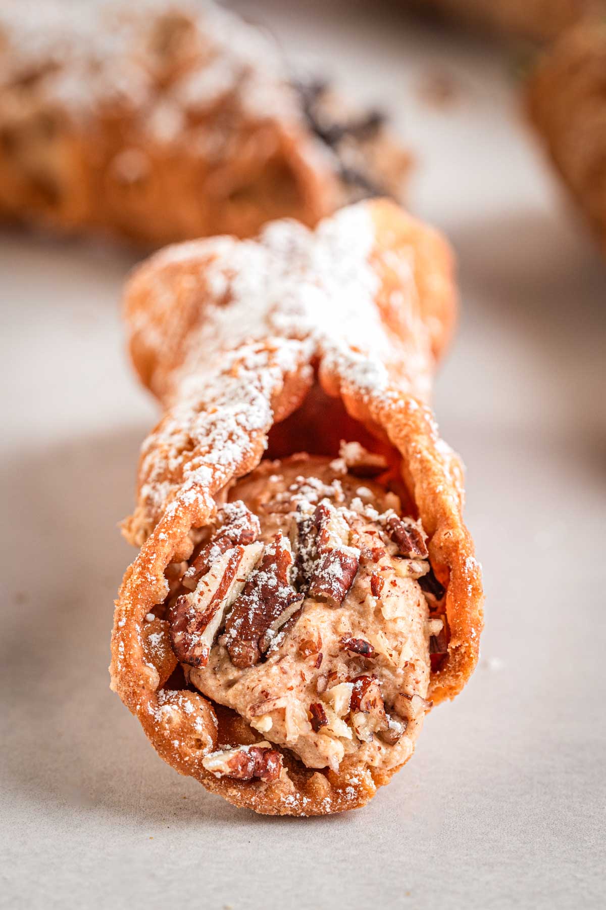 Close-up of one pumpkin cannoli filled with creamy pumpkin filling and chopped pecans, dusted with powdered sugar.