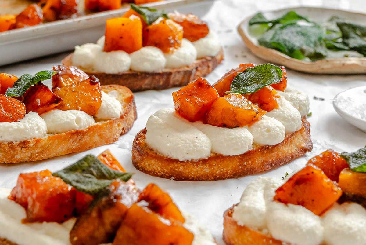 Side view of multiple pumpkin ricotta crostini on toasted bread slices, showing the contrast between golden crust, whipped ricotta, and roasted pumpkin.