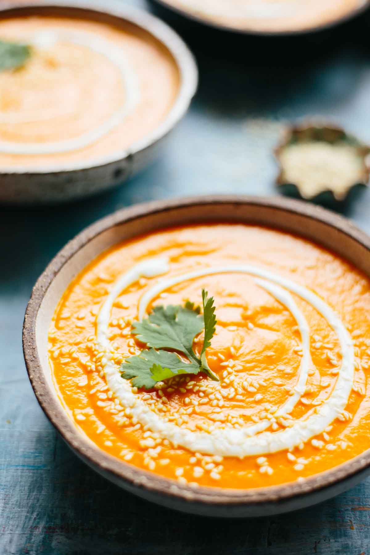 Close-up of a bowl of spicy carrot soup garnished with sesame seeds, cilantro, and a drizzle of yogurt.