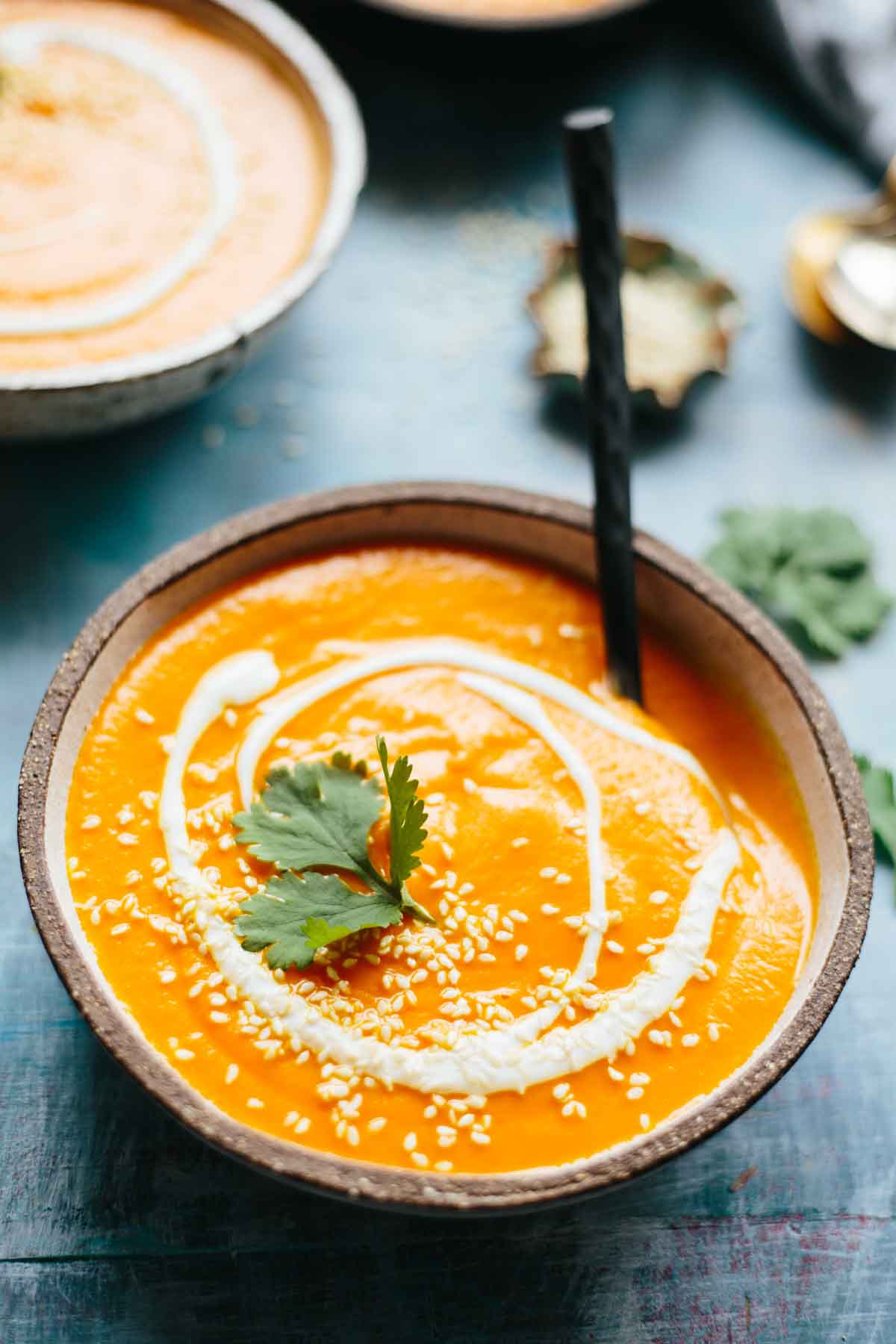 Overhead view of a bowl of spicy carrot soup with yogurt swirl and cilantro, served with a spoon.