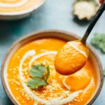 A spoonful of silky spicy carrot soup lifted from a bowl, showing its creamy texture and vibrant orange color.
