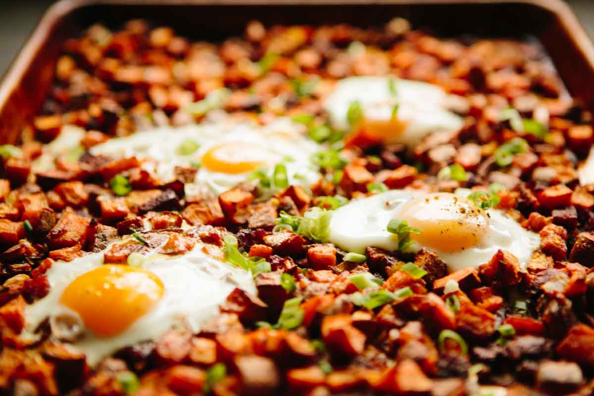 Close-up of sheet pan sweet potato and chorizo hash topped with sunny-side-up eggs and sprinkled with chopped scallions