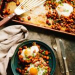 Overhead view of a baking sheet filled with roasted sweet potatoes, chorizo, and baked eggs, with a serving plate nearby.