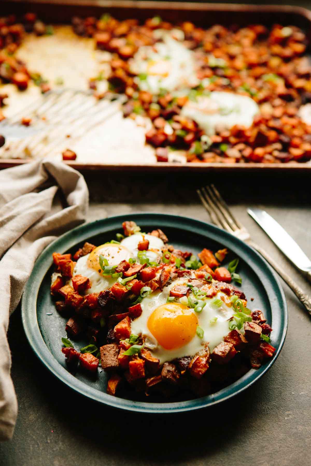 Sweet potato and chorizo hash served on a dark plate with eggs on top and a fork beside it.