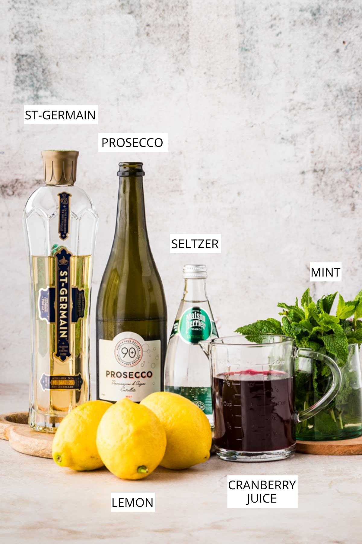 Labeled ingredients for Cranberry Hugo Spritz including St-Germain elderflower liqueur, prosecco, seltzer, mint, lemons, and cranberry juice.