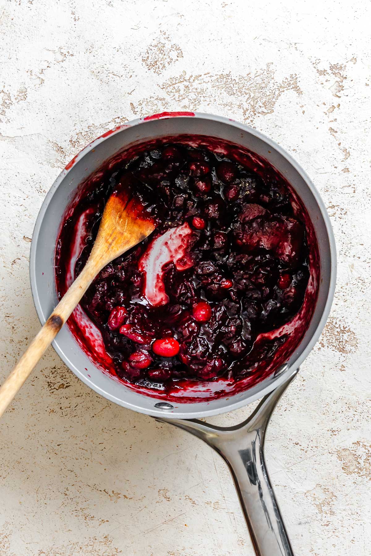 Cranberry sauce cooking in a saucepan with a wooden spoon, showing the thick, jammy texture as the cranberries break down.