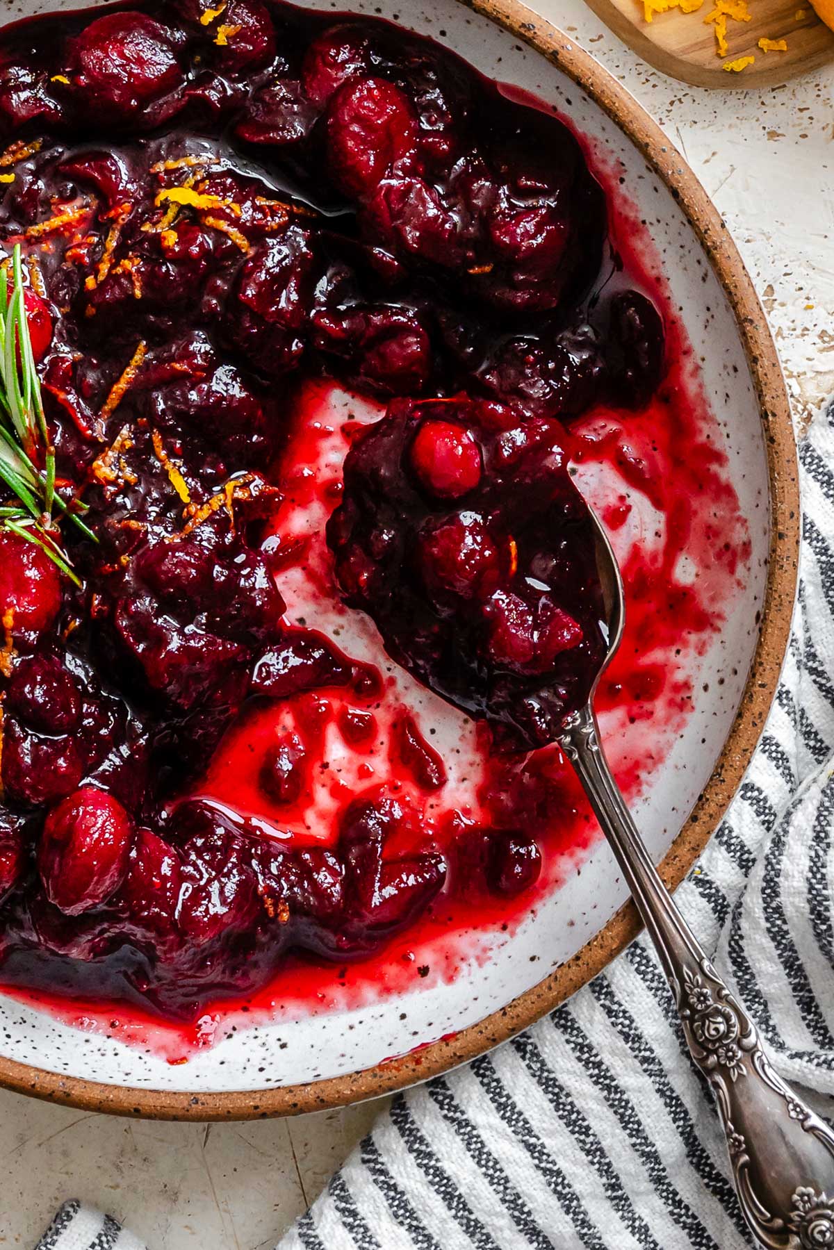 Close-up of thick, glistening cranberry sauce in a bowl with a spoonful lifted, highlighting the whole cranberries and deep red color.