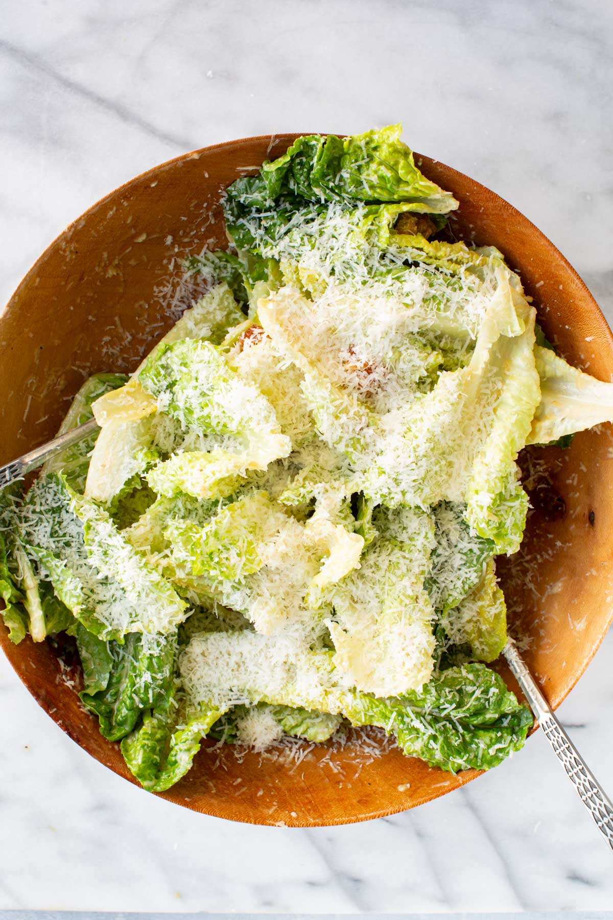 Crisp romaine leaves tossed in creamy Caesar dressing, topped generously with finely grated parmesan inside a large wooden bowl.