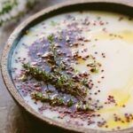 A close up of the soup showing the silky texture, glossy olive oil, scattered quinoa and fresh thyme leaves along the edge of the bowl.