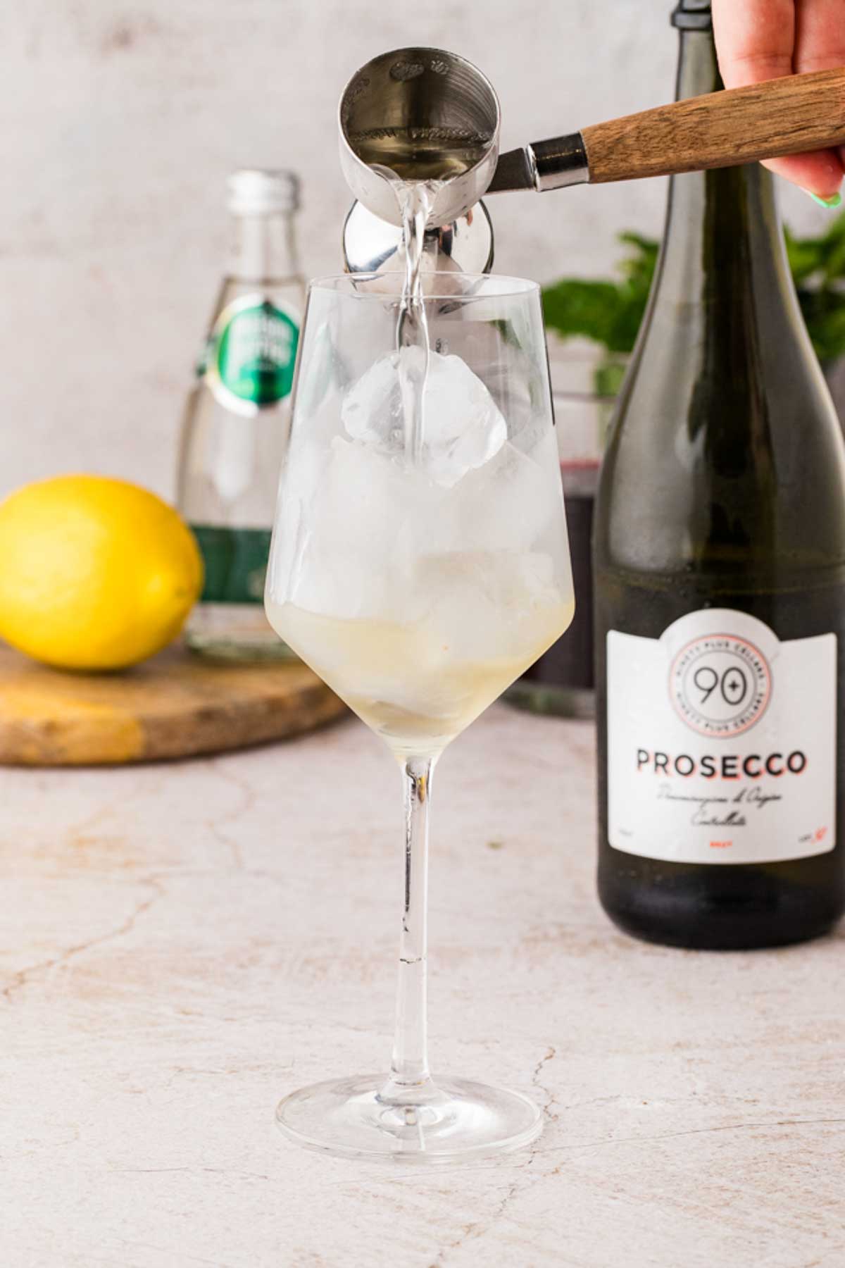 Adding prosecco to a chilled wine glass over ice while preparing a Cranberry Hugo Spritz.