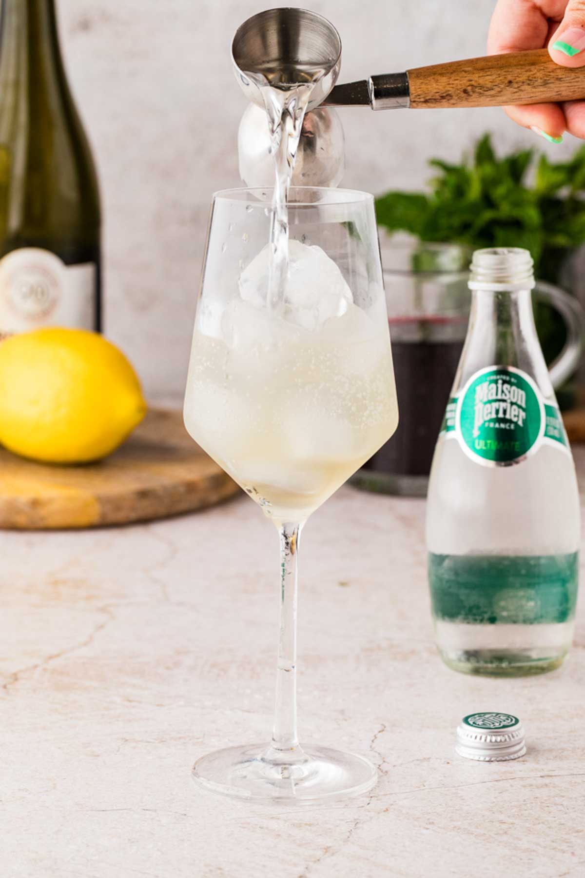 Pouring sparkling seltzer into a glass with prosecco and elderflower liqueur to make a Cranberry Hugo Spritz.