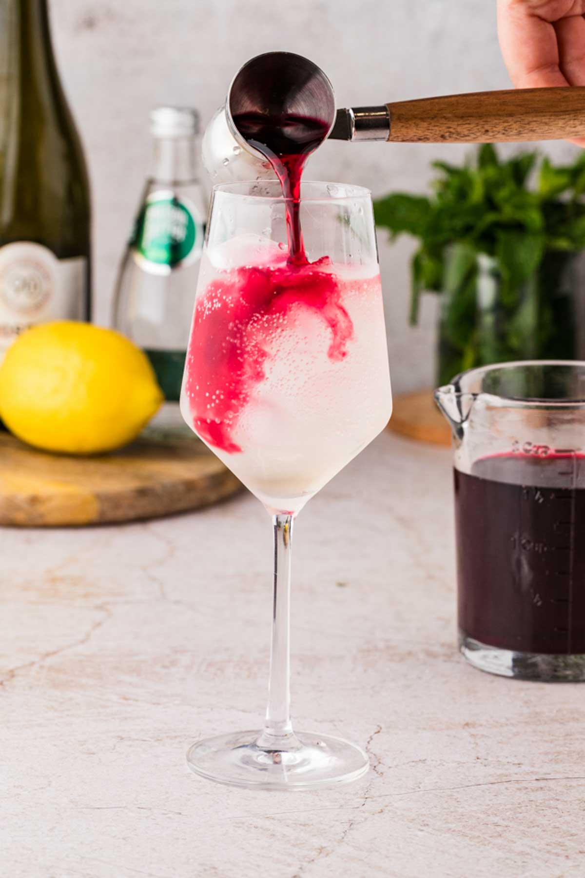 Cranberry juice being poured into the glass, swirling through the pale cocktail to create a pink ombré effect.