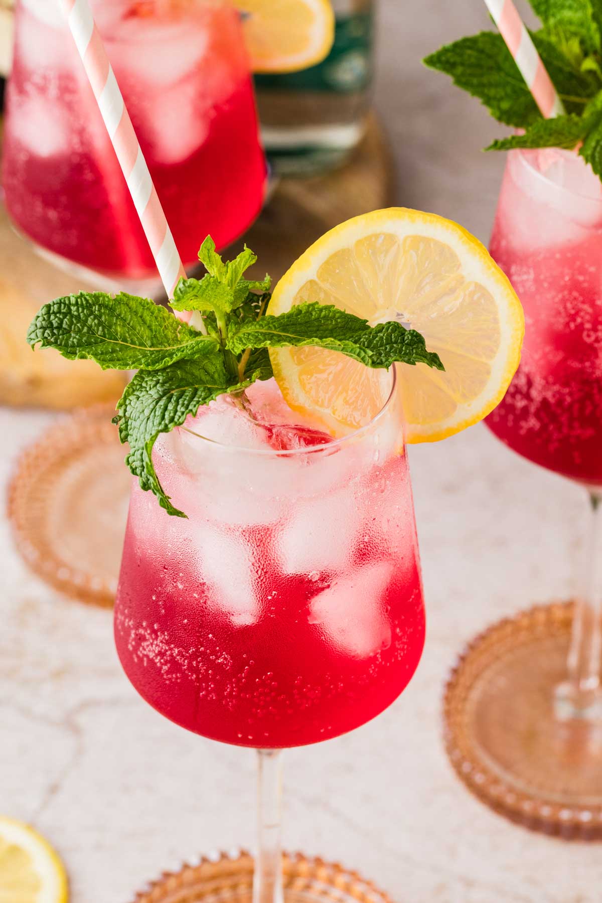Close-up of a Cranberry Hugo Spritz with a pink straw, fresh mint, and a lemon slice on top of crushed ice.