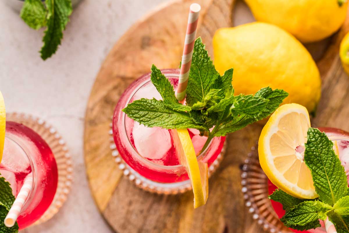 Overhead view of Cranberry Hugo Spritz cocktails on a wooden board with lemons and fresh mint leaves.
