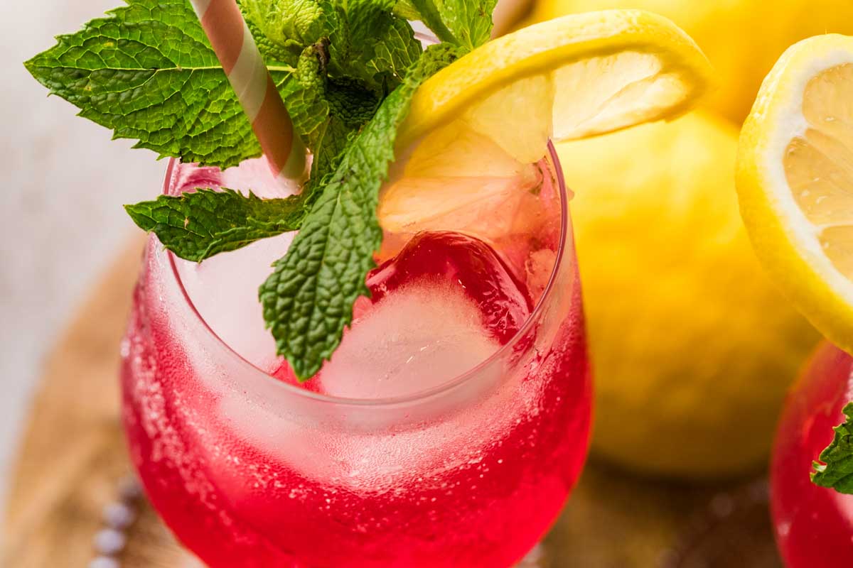Detailed close-up of a Cranberry Hugo Spritz highlighting condensation, mint garnish, and bright lemon slice.