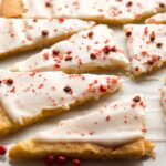 Iced grapefruit shortbread triangles scattered across parchment paper, each piece topped with crushed pink peppercorns for texture and color.