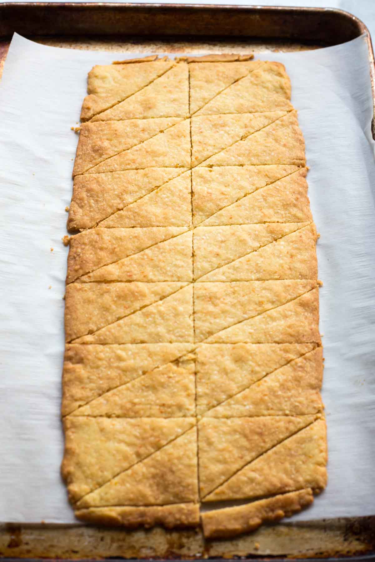 A full sheet of plain baked shortbread cut into triangular pieces, golden brown and still on the parchment lined baking sheet.