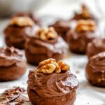 Frosted chocolate spice cookies arranged on parchment paper, each topped with a walnut half.