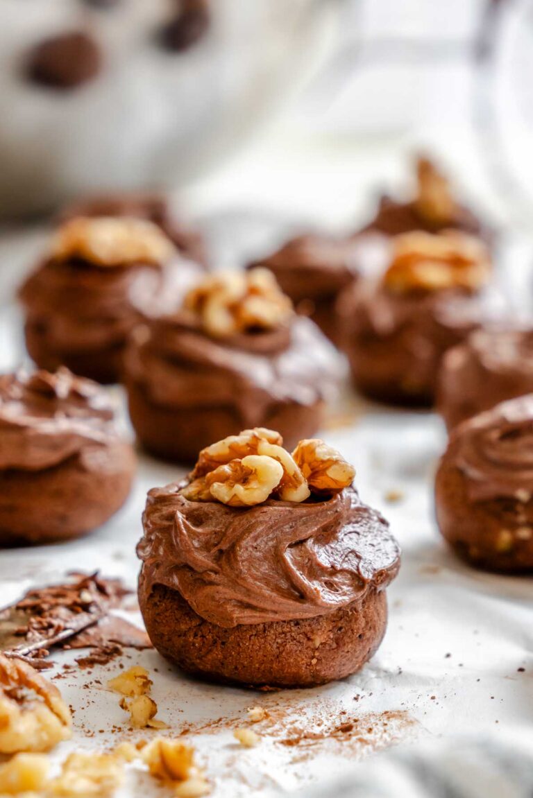 Frosted chocolate spice cookies arranged on parchment paper, each topped with a walnut half.