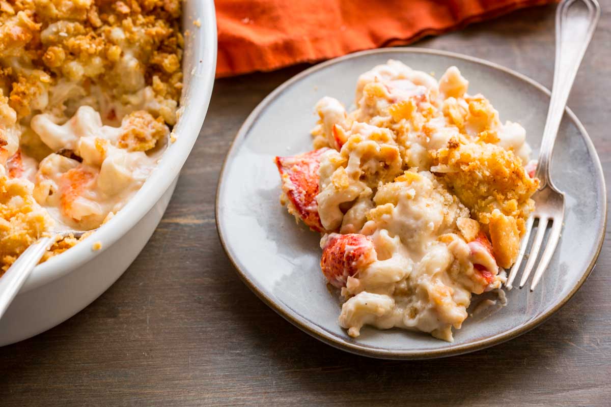 A plate of lobster mac and cheese next to the baking dish with visible chunks of lobster and creamy sauce.