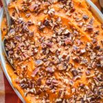 Top-down image of smooth sweet potato casserole garnished with crunchy toasted pecans on a plaid fall tablecloth.