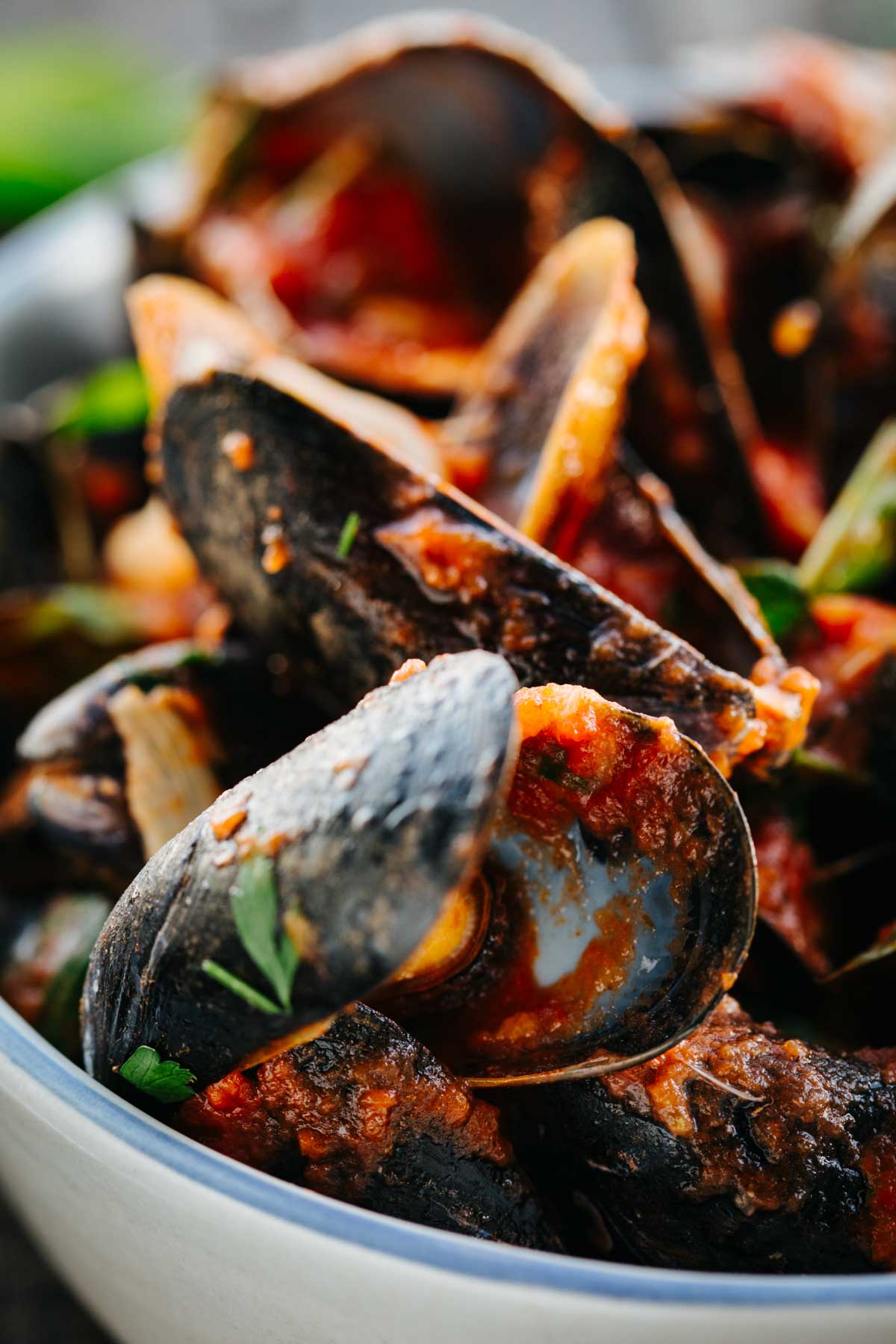 A tight close up of mussels coated in tomato sauce, showing the texture of the shells and fresh herbs.