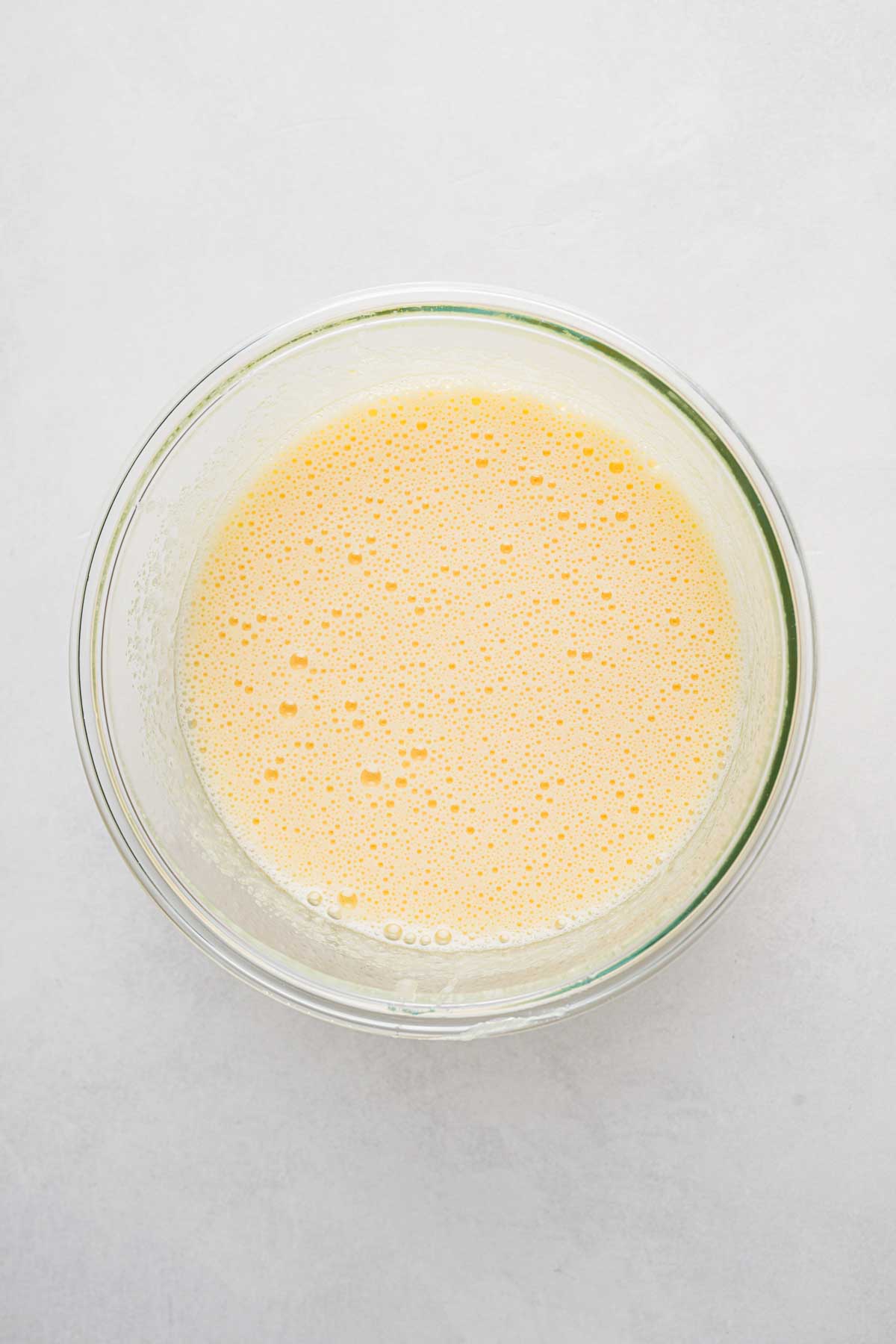 Light, frothy mixture of beaten eggs and sugar in a clear glass bowl on a light surface.