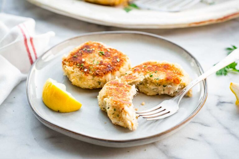 Two mashed potato fish cakes on a plate with one broken open to show the flaky interior, with a lemon wedge and fork on the side.