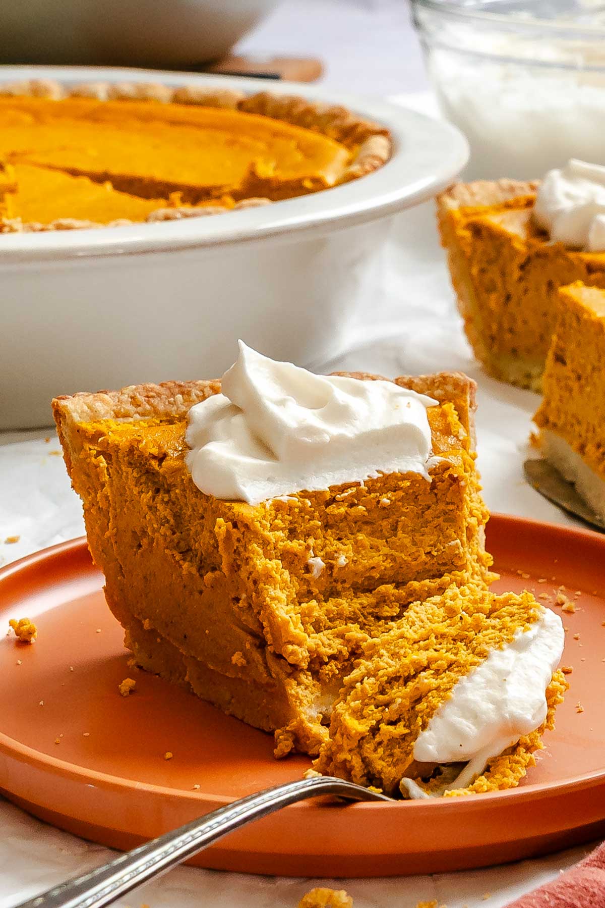 Side view of a thick slice of pumpkin ricotta pie showing creamy texture and flaky crust, topped with whipped cream.
