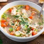 Close-up of turkey orzo soup showing vegetables, shredded turkey and chopped parsley.