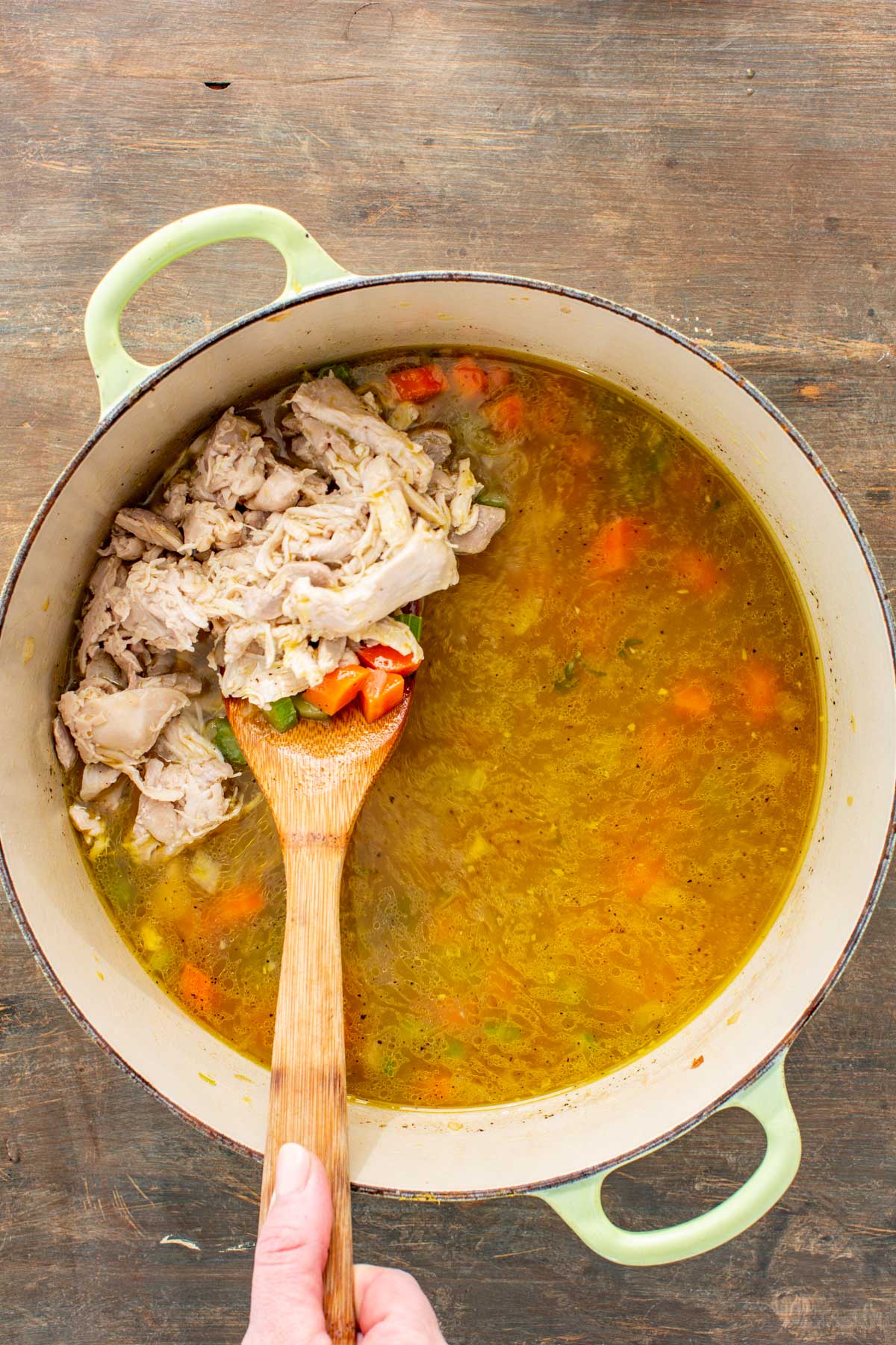 Shredded cooked turkey being stirred into the pot of simmering broth and vegetables.