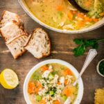 A bowl of turkey orzo soup served with slices of crusty bread, lemon and parsley on the side.
