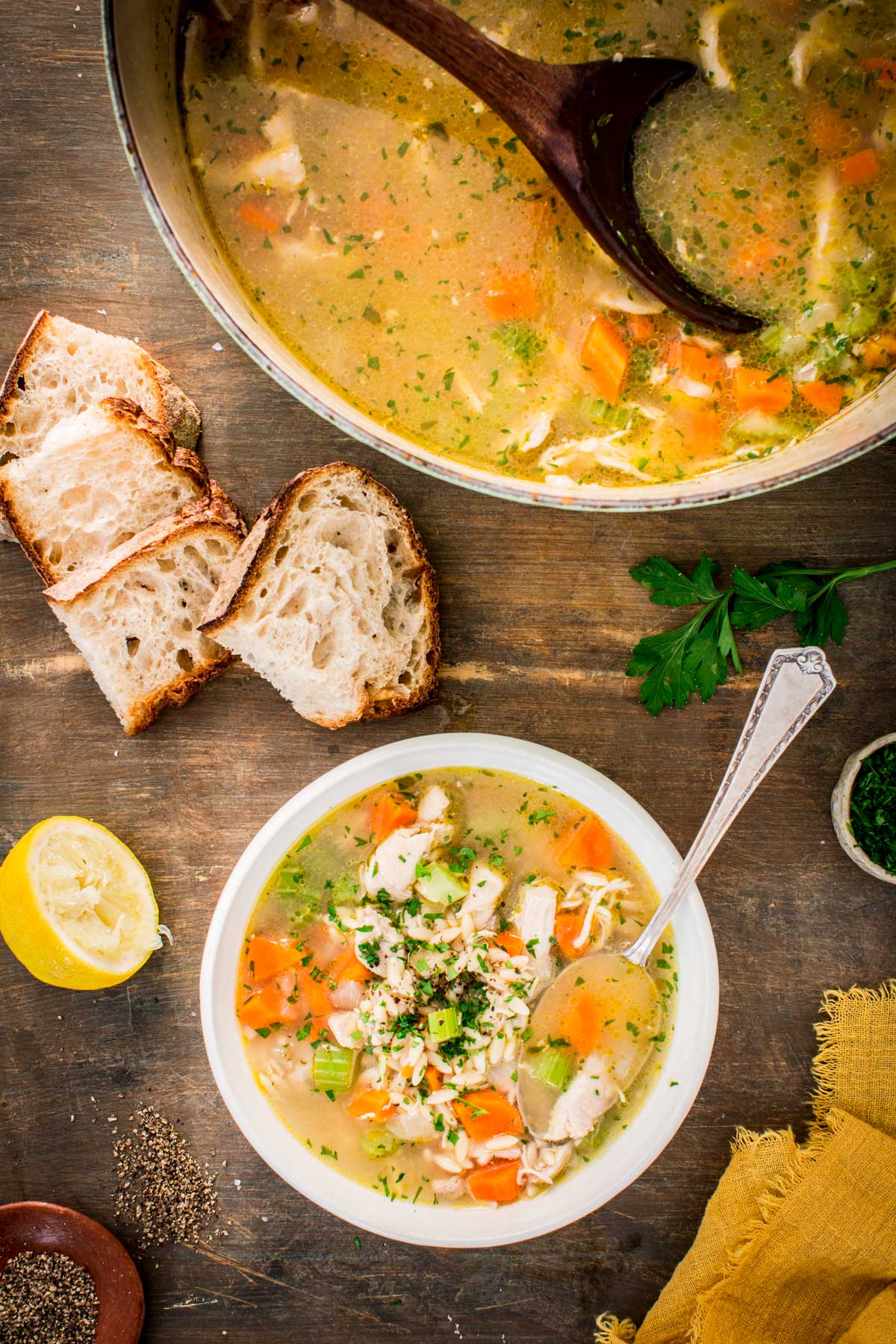 A bowl of turkey orzo soup served with slices of crusty bread, lemon and parsley on the side.
